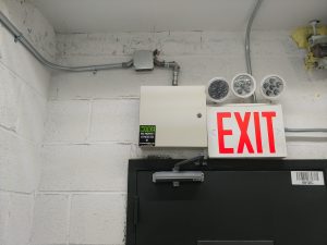 Wall mounted DVR locked box next to lighted exit sign above a door frame